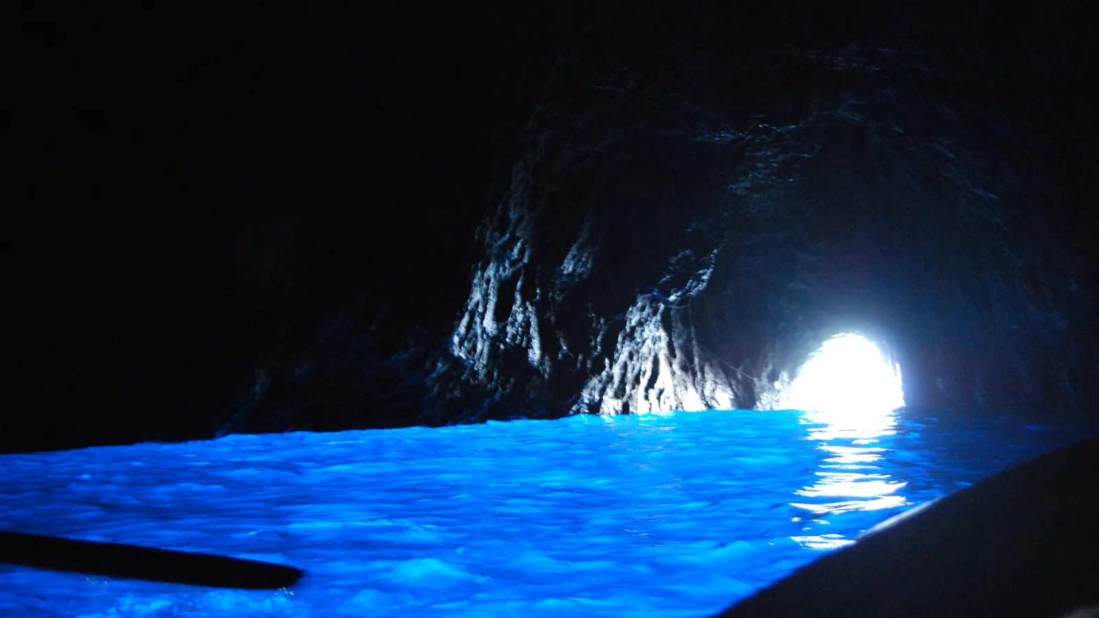 Leuchtend blaues Wasser im Inneren der Blauen Grotte auf Capri, hinten der helle Eingang